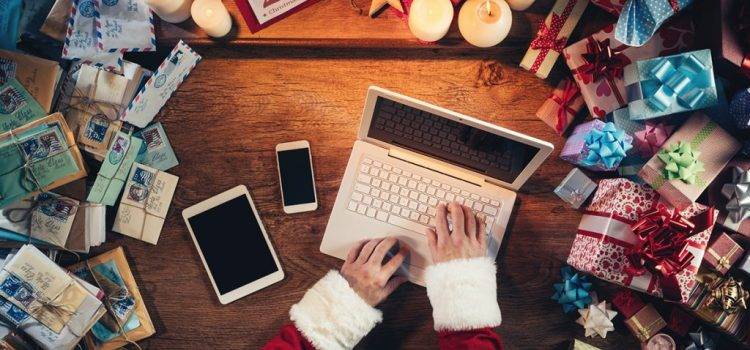 Papai noel utilizando laptop numa mesa com várias cartas e presentes de Natal